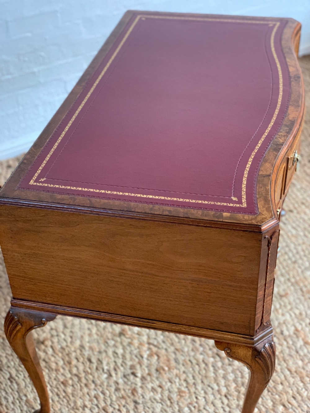An early 20th-century burr walnut writing desk featuring five drawers with brass handles, carved cabriole legs, and a fitted kneehole. View VIII