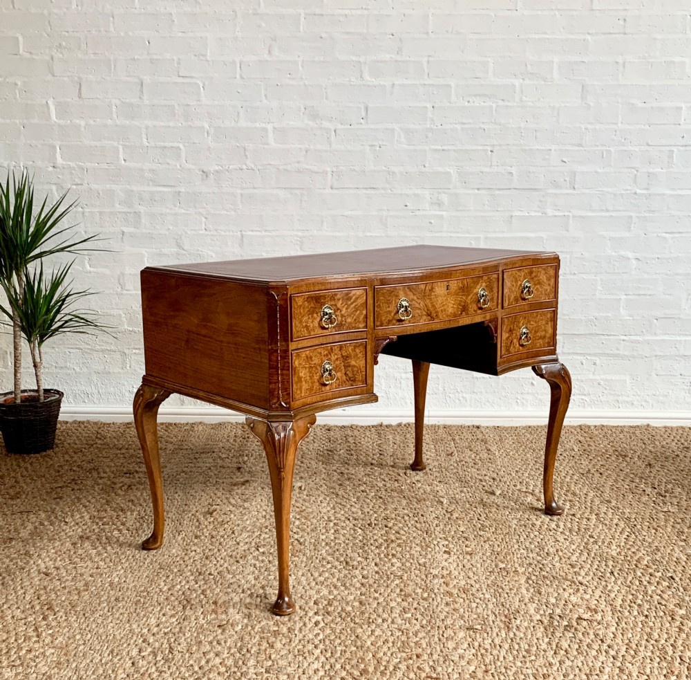 An early 20th-century burr walnut writing desk featuring five drawers with brass handles, carved cabriole legs, and a fitted kneehole.