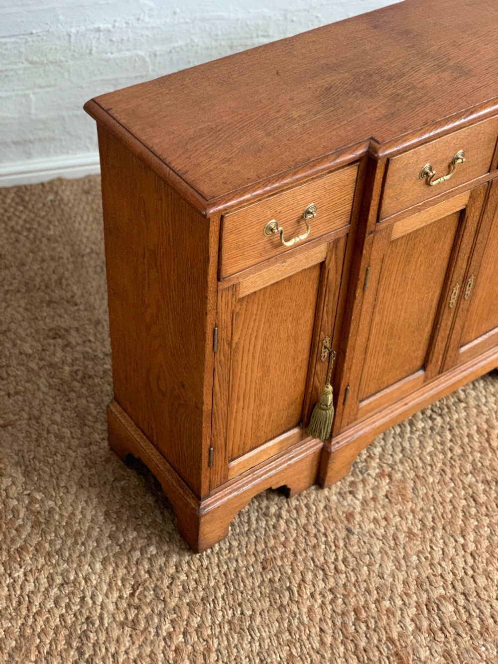 A golden oak sideboard featuring four upper drawers, four panelled cupboard doors with brass handles, keyhole escutcheons with tassels, and bracket feet. View IV