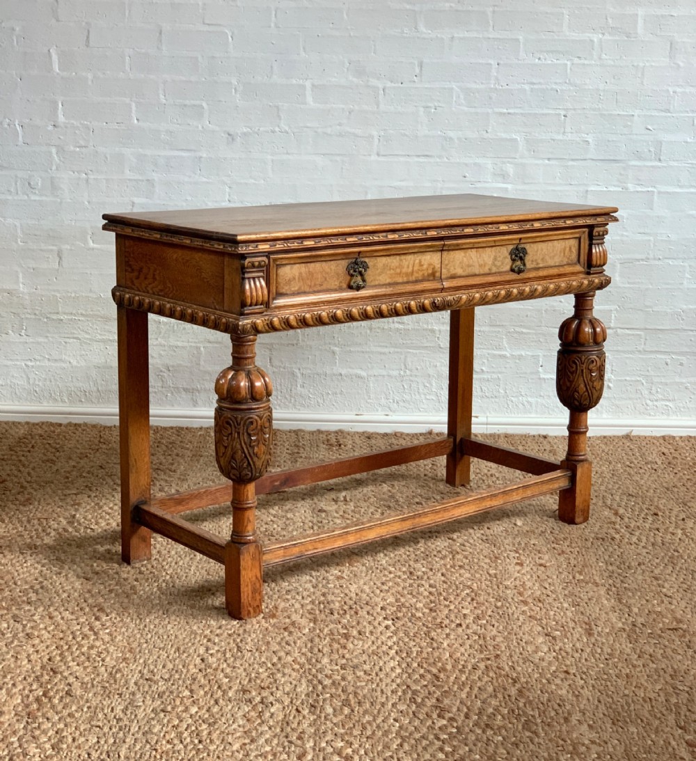 A 1920s carved oak side serving table with two drawers, brass handles, carved bulbous front legs, and a lower stretcher frame.