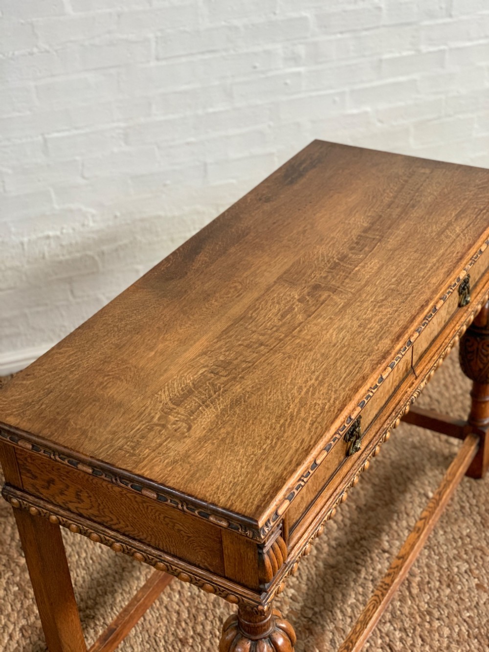 A 1920s carved oak side serving table with two drawers, brass handles, carved bulbous front legs, and a lower stretcher frame. View V