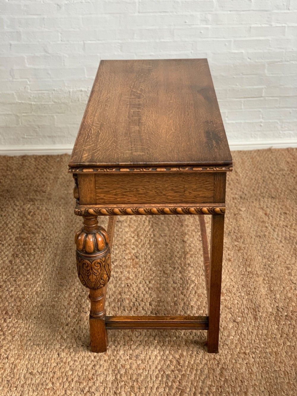A 1920s carved oak side serving table with two drawers, brass handles, carved bulbous front legs, and a lower stretcher frame. View XI