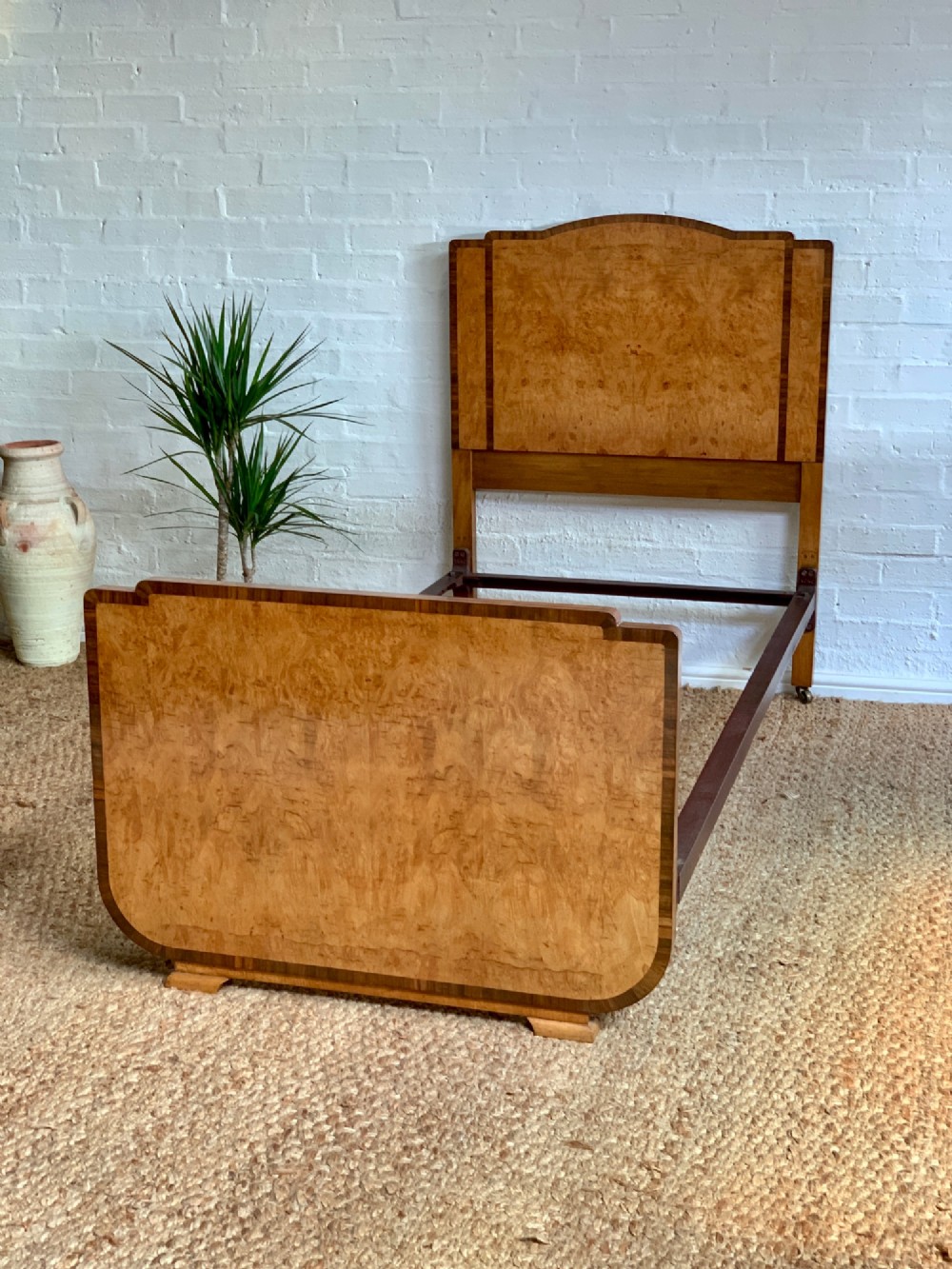 An Art Deco single bed frame crafted from figured burr walnut veneer with crossbanded borders, featuring a gently arched headboard and rounded footboard.