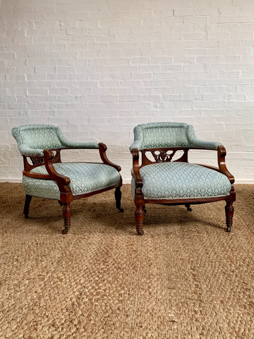 A pair of Edwardian walnut tub armchairs with pale blue patterned upholstery, turned front legs, and castors.