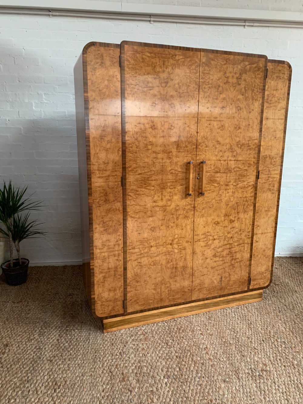 An Art Deco double wardrobe crafted from figured burr walnut veneer with rounded top edges, vertical wooden handles, and a stepped plinth base. View IX