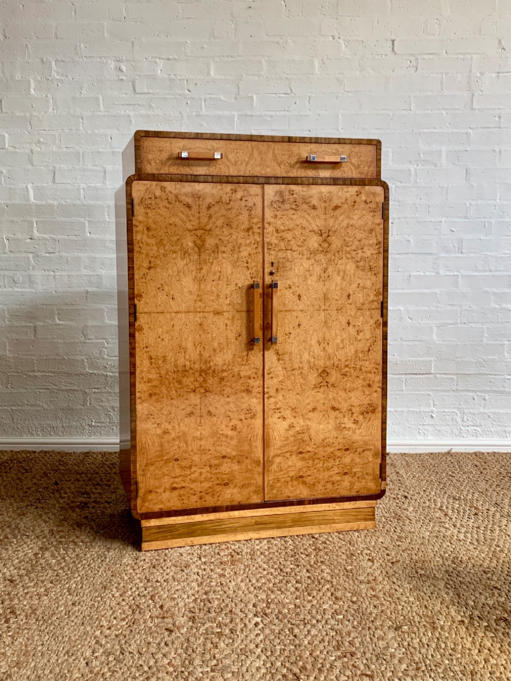 An Art Deco tallboy made from book-matched burr walnut, featuring a top drawer over a two-door cabinet on a stepped plinth base.