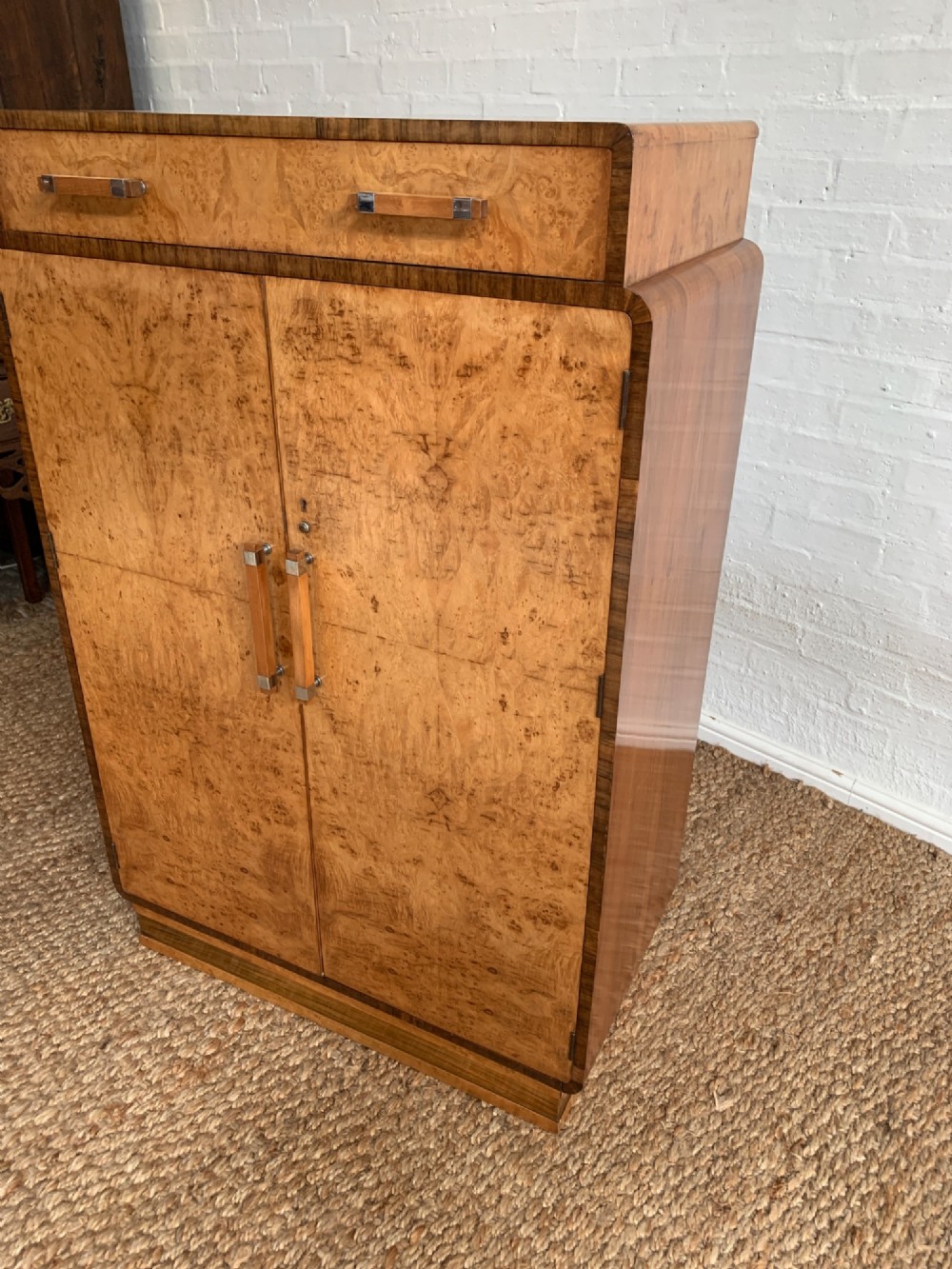 An Art Deco tallboy made from book-matched burr walnut, featuring a top drawer over a two-door cabinet on a stepped plinth base. View V