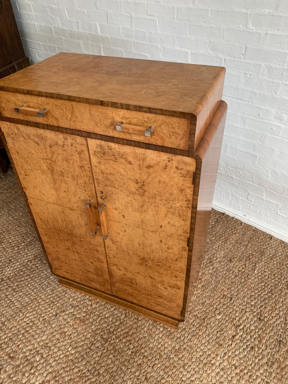 An Art Deco tallboy made from book-matched burr walnut, featuring a top drawer over a two-door cabinet on a stepped plinth base. View VI