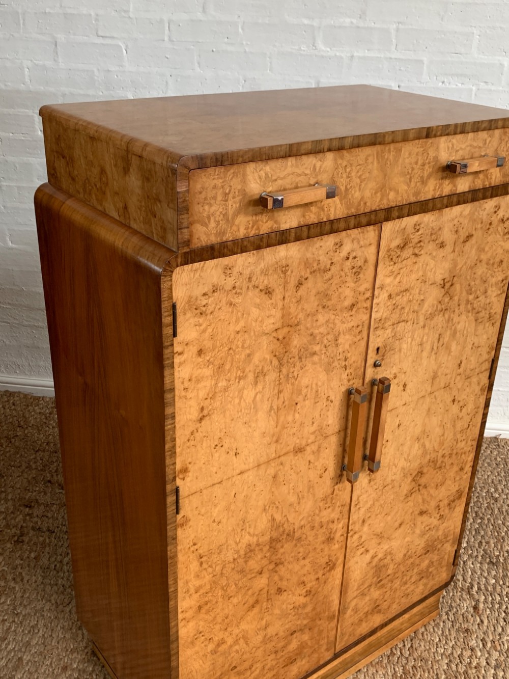 An Art Deco tallboy made from book-matched burr walnut, featuring a top drawer over a two-door cabinet on a stepped plinth base. View X