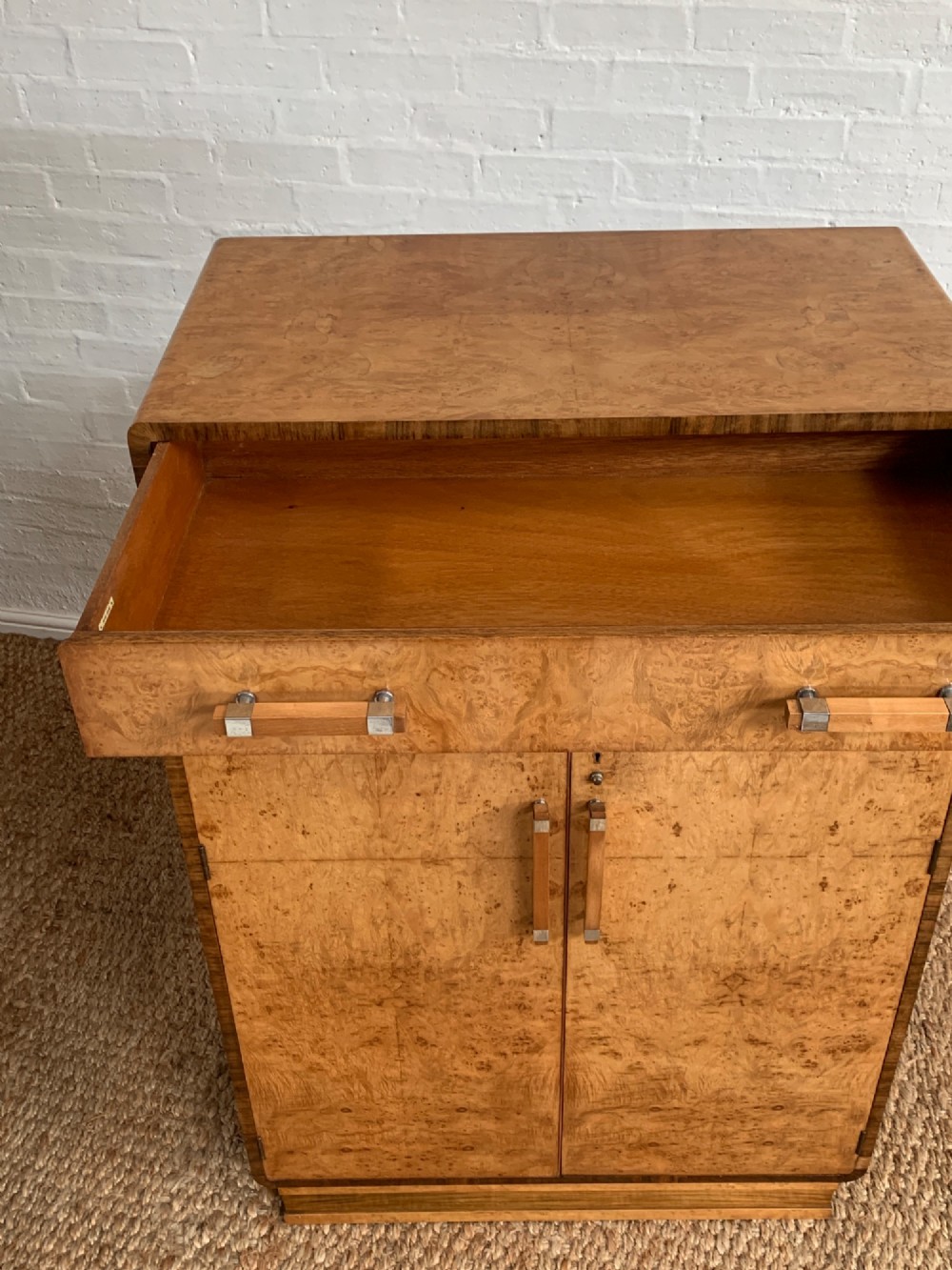 An Art Deco tallboy made from book-matched burr walnut, featuring a top drawer over a two-door cabinet on a stepped plinth base. View XII