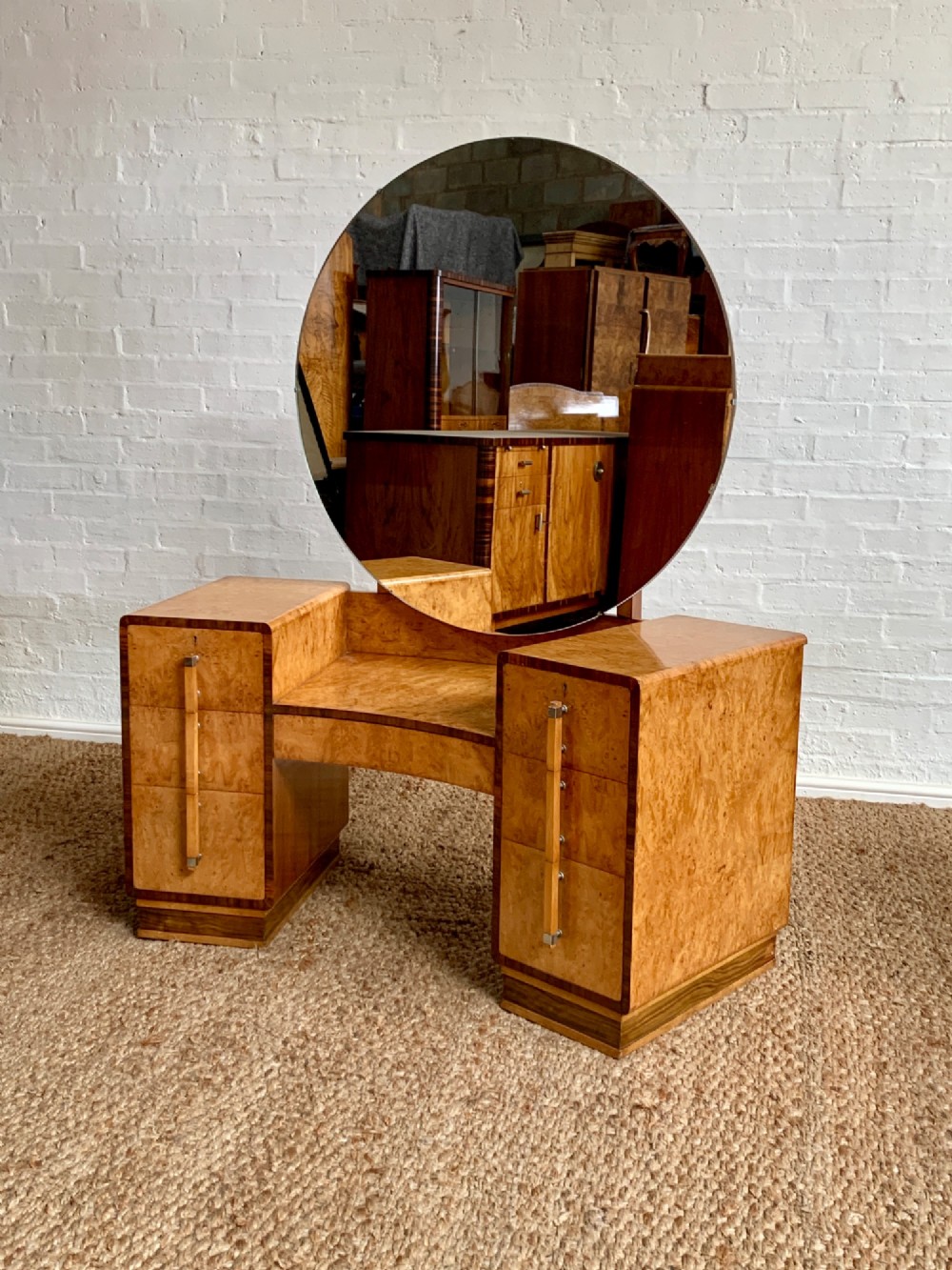 An Art Deco burr walnut dressing table featuring a circular mirror, twin pedestals, and vertical drawer handles.