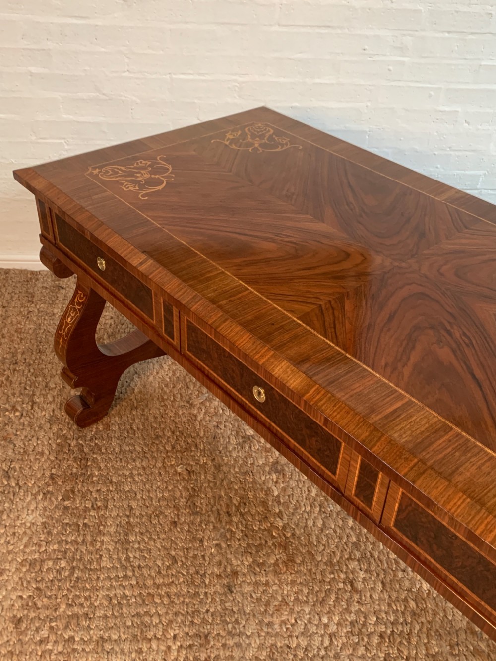 A rectangular walnut writing desk featuring decorative corner marquetry, three frieze drawers with brass pulls, curved lyre-shaped legs, and a shaped central stretcher. View III