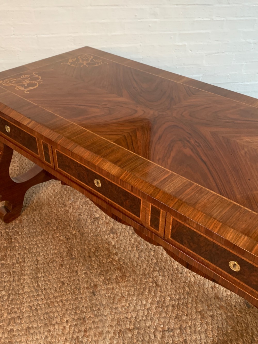 A rectangular walnut writing desk featuring decorative corner marquetry, three frieze drawers with brass pulls, curved lyre-shaped legs, and a shaped central stretcher. View V