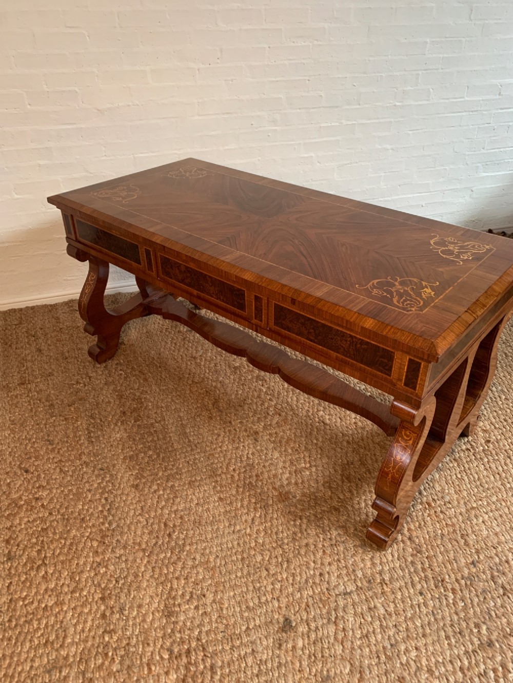A rectangular walnut writing desk featuring decorative corner marquetry, three frieze drawers with brass pulls, curved lyre-shaped legs, and a shaped central stretcher. View X