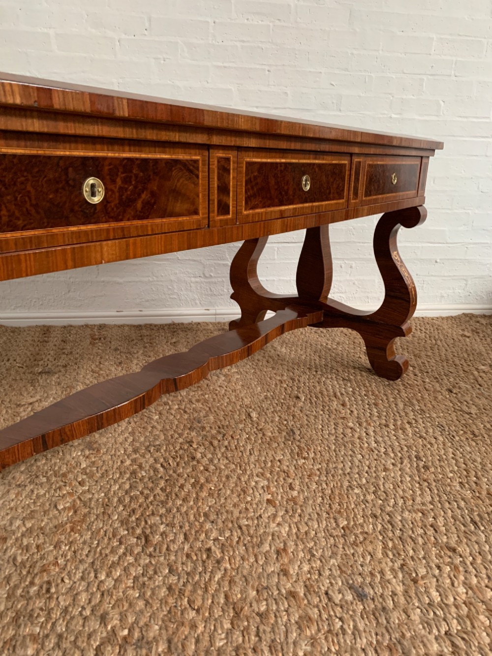 A rectangular walnut writing desk featuring decorative corner marquetry, three frieze drawers with brass pulls, curved lyre-shaped legs, and a shaped central stretcher. View XIII