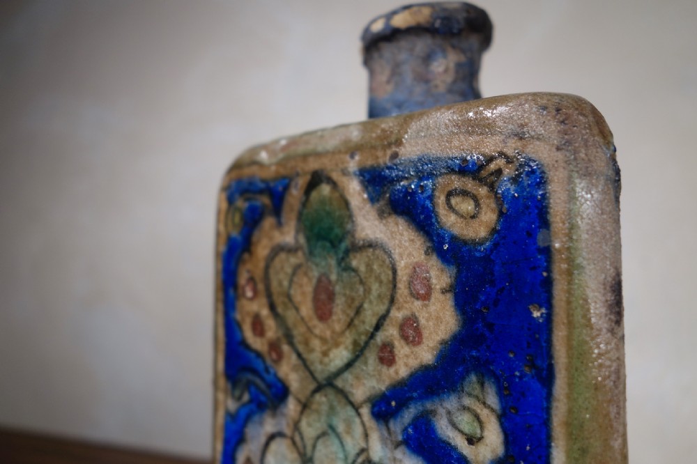 A triangular Persian glazed earthenware vessel decorated with cobalt blue, turquoise, and hand-painted arabesque motifs along its sides. View X