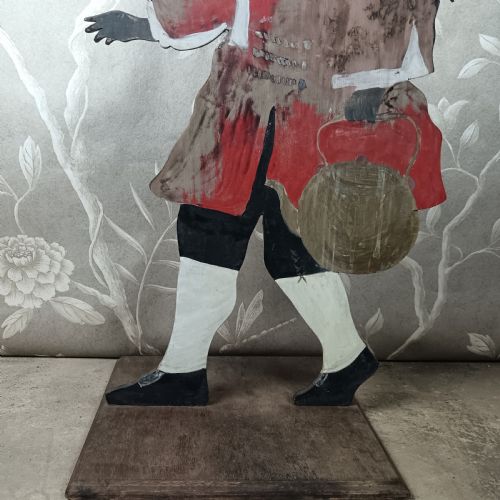 fig 3. An early twentieth-century painted wooden dummy board figure depicting a man in a red coat and feathered hat holding a kettle.