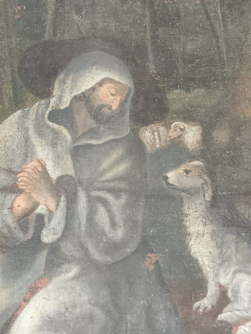 fig 2. An antique naive oil painting depicting Saint Francis kneeling in prayer amongst sheep in a wooded landscape within a grey painted frame.