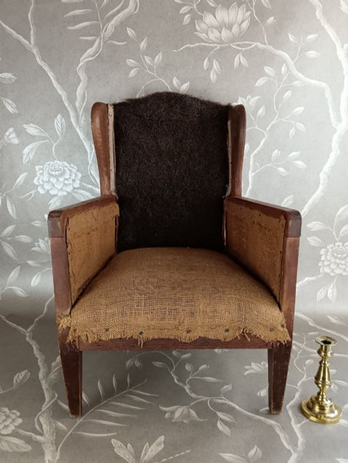 fig 1. An early 20th-century childs wingback armchair featuring an exposed timber frame, tapered legs, and visible hessian upholstery layer.