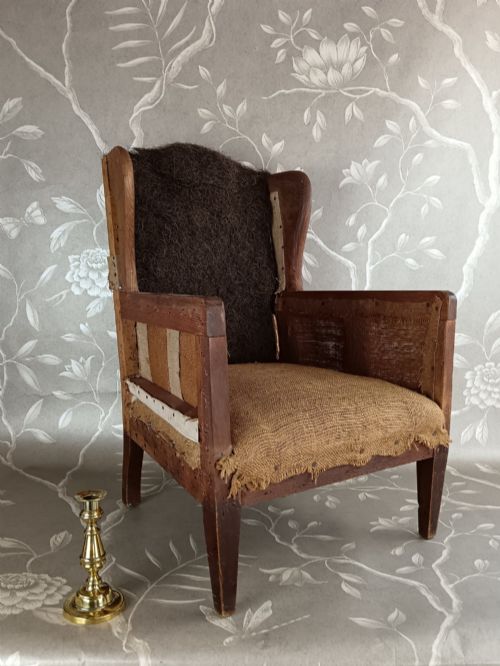 fig 2. An early 20th-century childs wingback armchair featuring an exposed timber frame, tapered legs, and visible hessian upholstery layer.