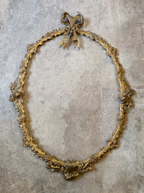 fig 2. An oval wall mirror framed in detailed gilt bronze with floral scrollwork and a prominent ribbon bow crest at the top.