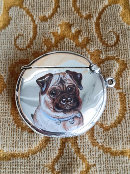 fig 1. A rounded silver vesta case featuring a finely painted enamel portrait of a pug dog on the front face.