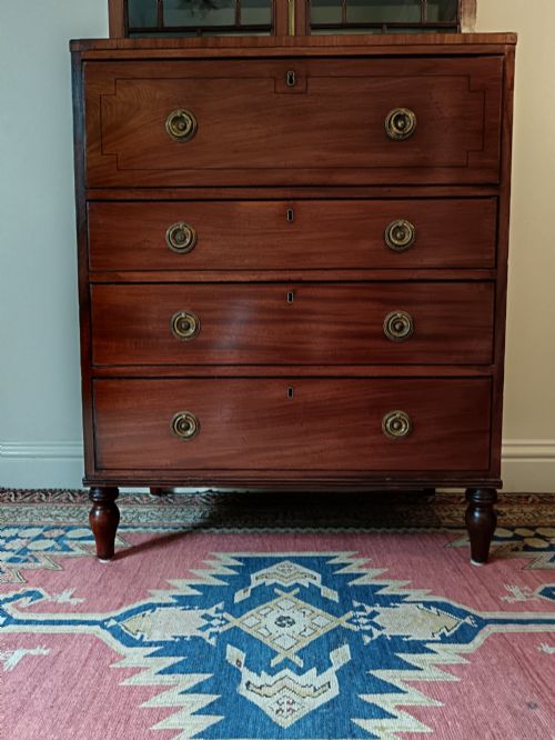 fig 4. A Regency mahogany secretaire cabinet featuring a triangular pediment top, glazed upper doors, a fall-front desk section, and three drawers below on turned feet.