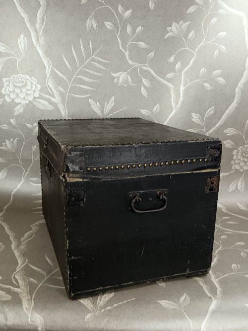 fig 1. A rectangular black leather travelling trunk featuring brass stud border detail, iron corner reinforcement brackets, and a brass central lock escutcheon.