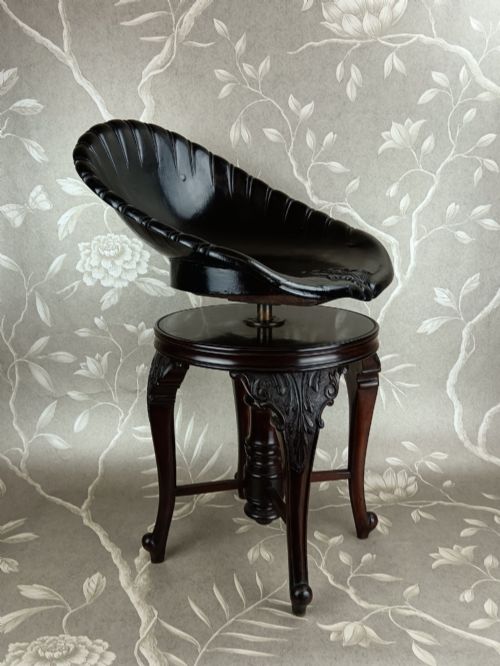 fig 2. A Victorian mahogany revolving music stool with a scalloped shell-shaped black backrest, turned central pedestal, and four carved legs.