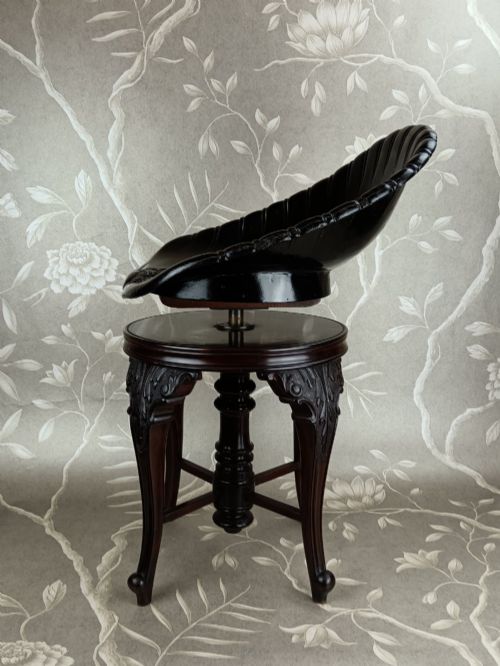 fig 3. A Victorian mahogany revolving music stool with a scalloped shell-shaped black backrest, turned central pedestal, and four carved legs.