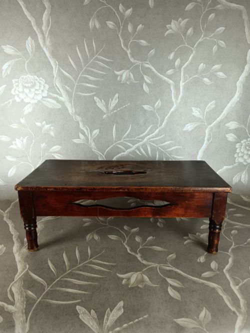 fig 1. A low 19th-century dark brown wooden footstool with turned legs, side cutouts, and a central carry handle slot on the top surface.