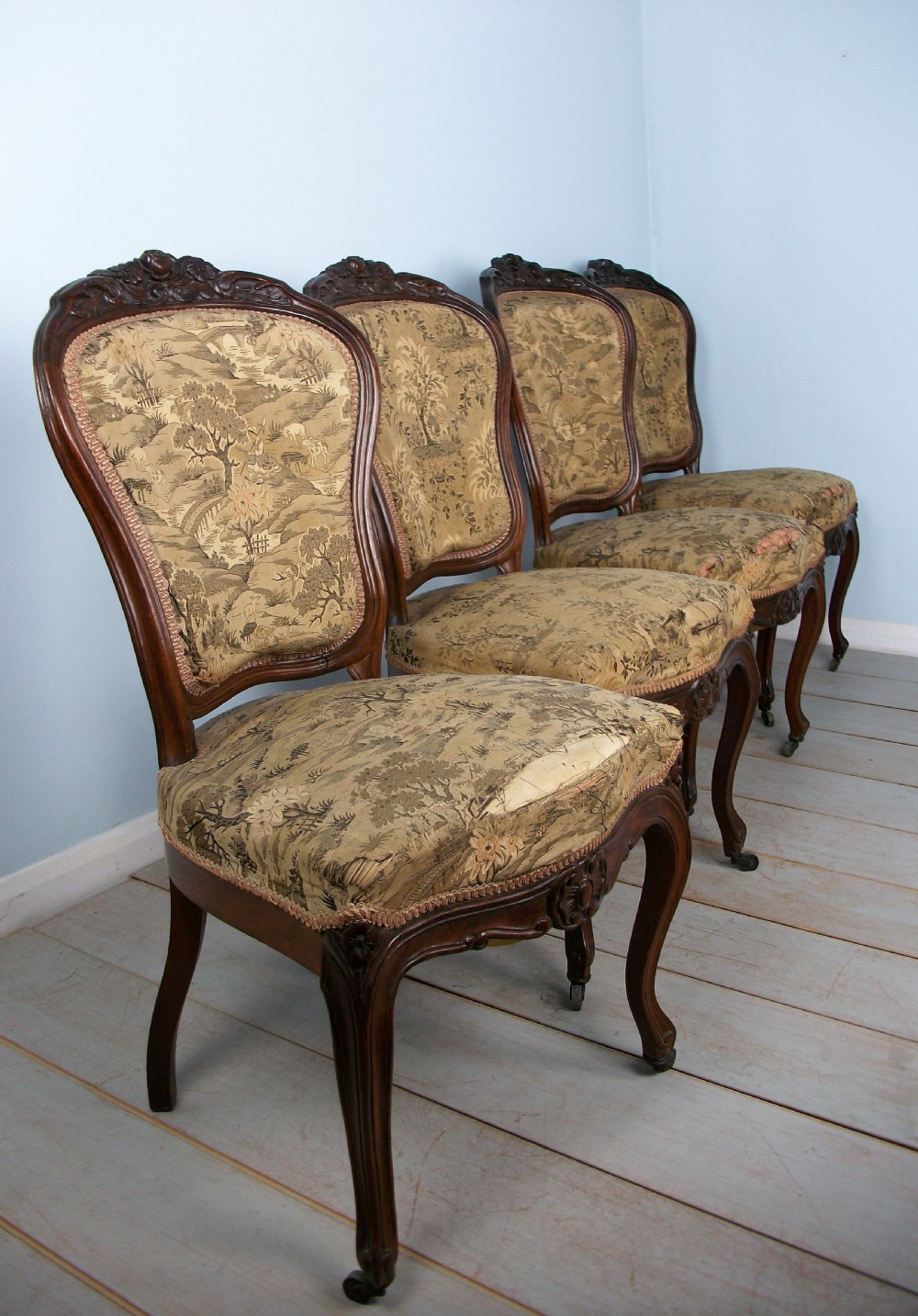 A set of four Victorian rosewood dining chairs featuring carved cartouche backs, patterned landscape upholstery, and cabriole legs on castors. View VIII