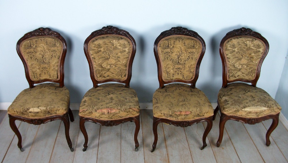 A set of four Victorian rosewood dining chairs featuring carved cartouche backs, patterned landscape upholstery, and cabriole legs on castors.