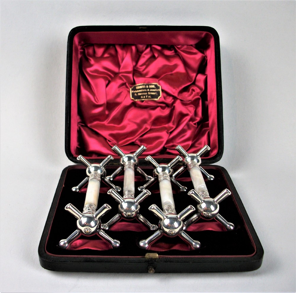 A set of four late Victorian silver-plated knife rests with mother-of-pearl central shafts displayed in an open silk-lined presentation box.