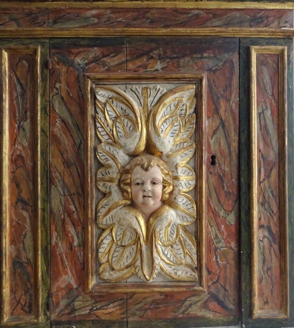 A rectangular Italian Baroque carved wood panel featuring a central gilded cherub head surrounded by leaf motifs, framed by faux-marbled painted sections and gilded mouldings. View VII