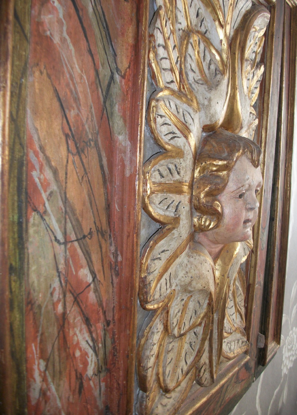 A rectangular Italian Baroque carved wood panel featuring a central gilded cherub head surrounded by leaf motifs, framed by faux-marbled painted sections and gilded mouldings. View VIII