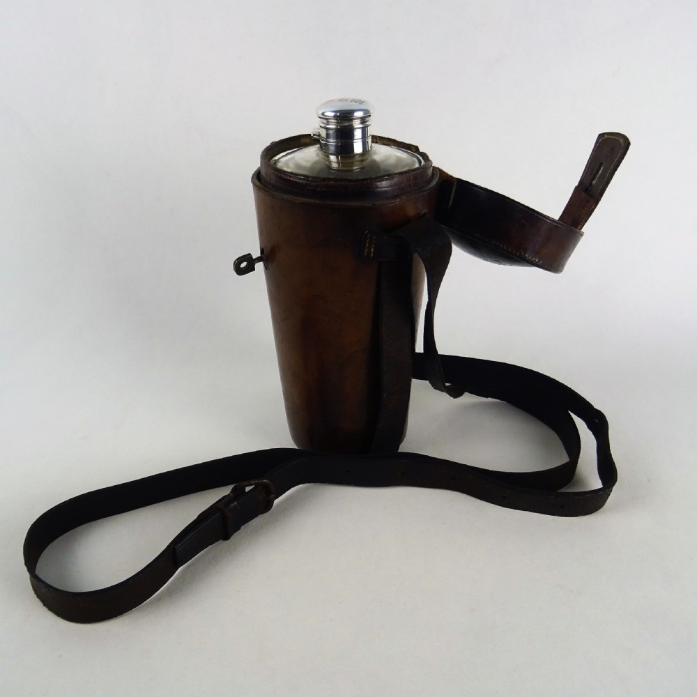 A nineteenth-century glass spirit flask encased in a dark brown leather carrying case with a leather shoulder strap and silver-toned metal cap.