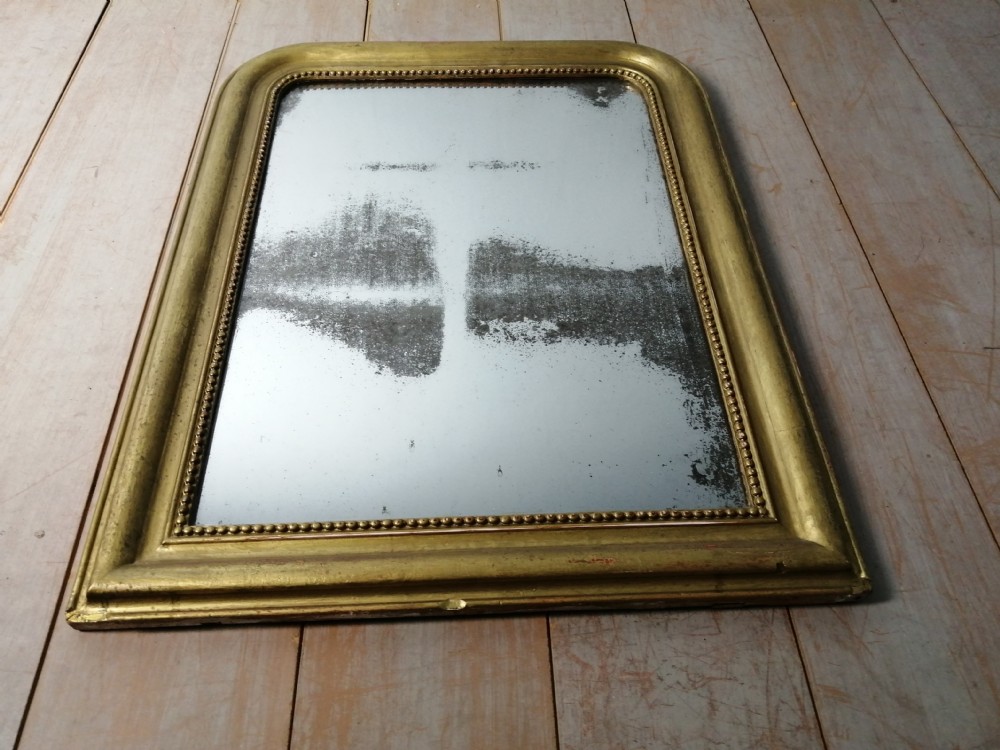A 19th-century French wall mirror featuring a rectangular gilded frame with rounded upper corners, beaded interior moulding, and heavily foxed glass. View V