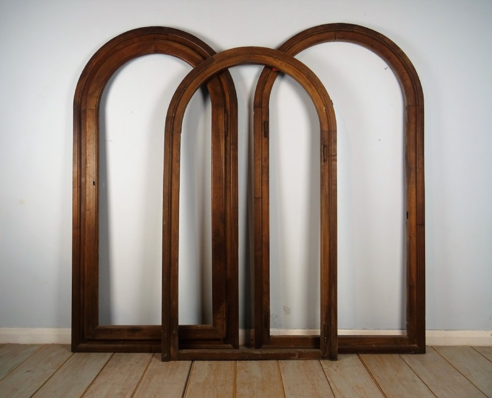 A group of three antique Italian walnut wooden door frames featuring rounded arches and moulded profiles.
