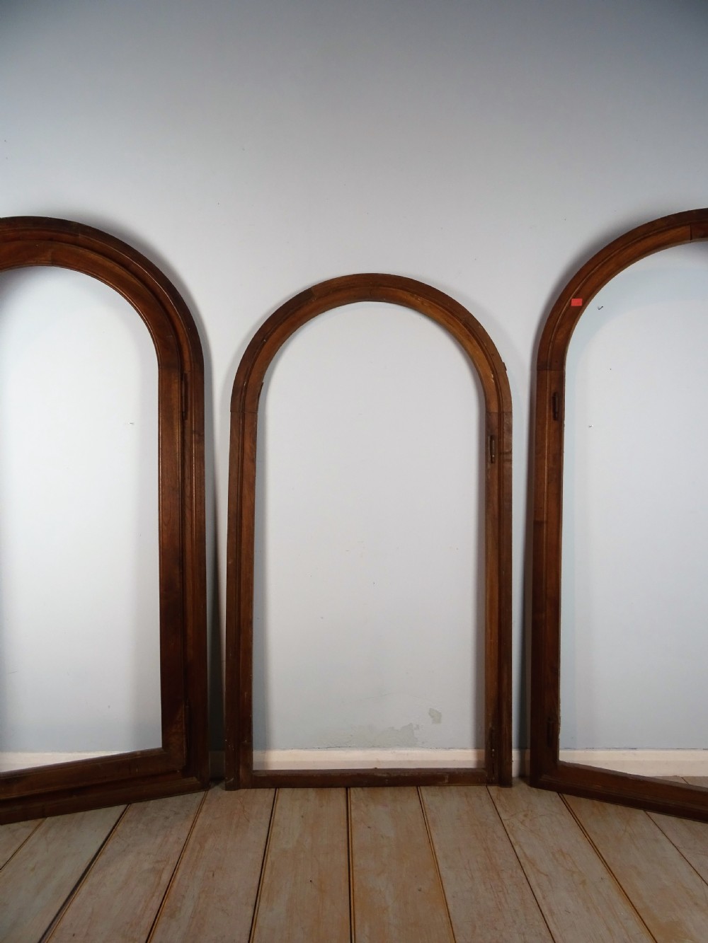 A group of three antique Italian walnut wooden door frames featuring rounded arches and moulded profiles. View II