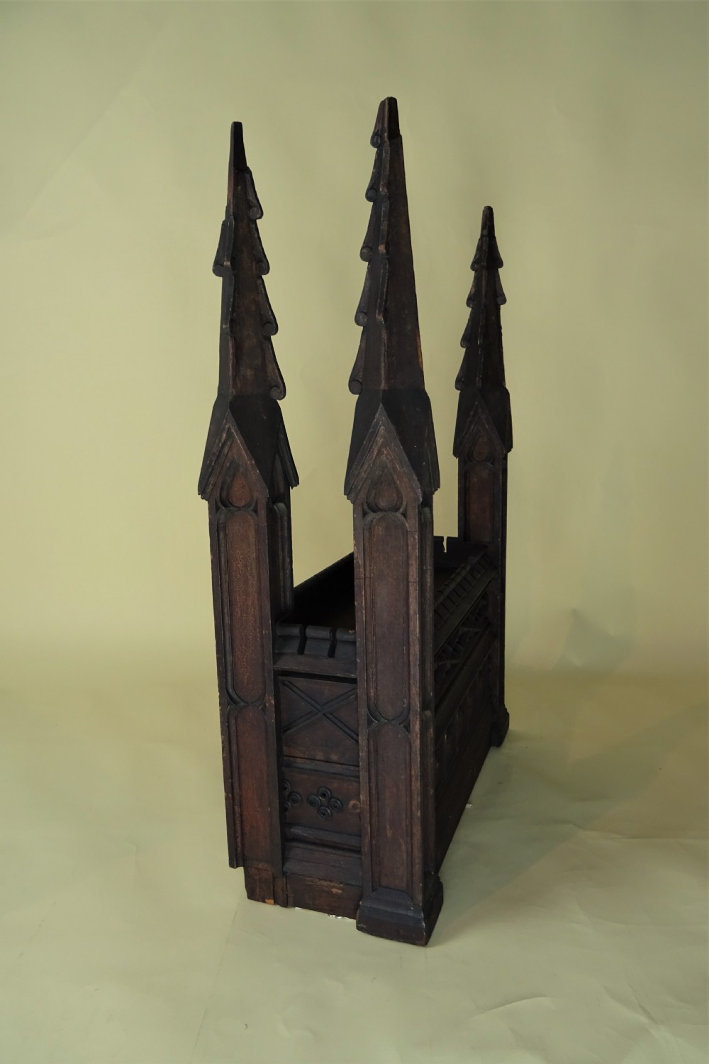A dark carved oak Gothic architectural element featuring four corner spires with crocketed details, crenellated upper edges, and geometric tracery relief panels. View XIV