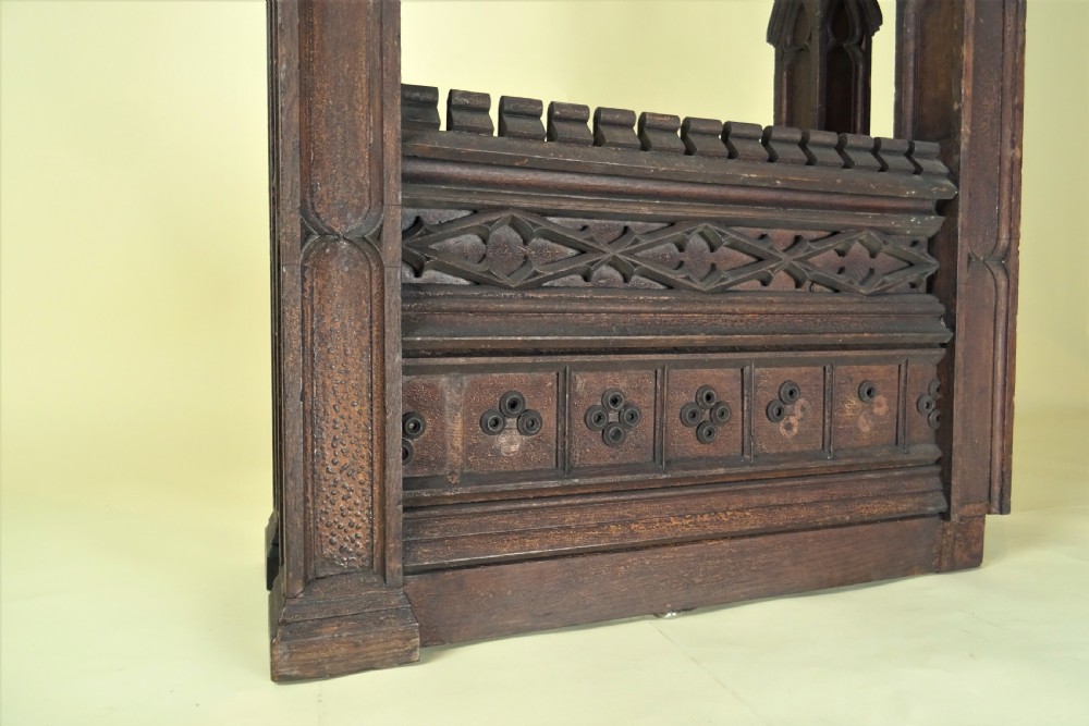 A dark carved oak Gothic architectural element featuring four corner spires with crocketed details, crenellated upper edges, and geometric tracery relief panels. View VII