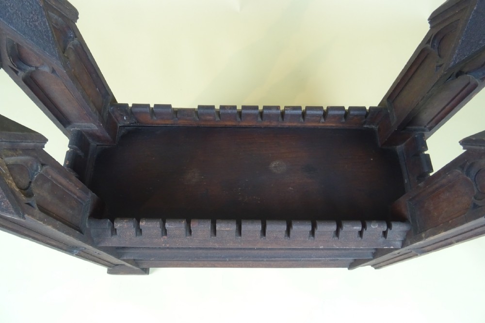 A dark carved oak Gothic architectural element featuring four corner spires with crocketed details, crenellated upper edges, and geometric tracery relief panels. View VIII