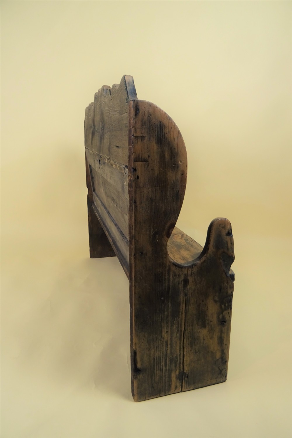 A miniature antique wooden pine settle featuring a scalloped top crest, solid seat, shaped winged sides, and a rustic weathered patina. View III
