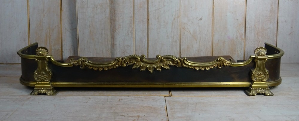A 19th-century brass and dark steel fireplace fender featuring cast brass Rococo scrollwork and shell motifs along the top rail and corner feet.