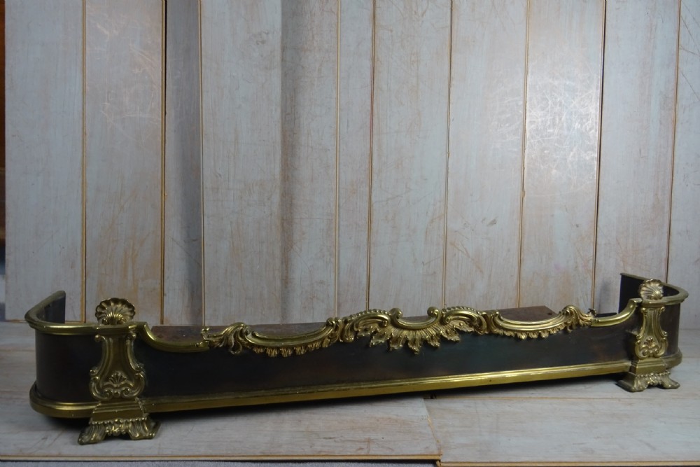 A 19th-century brass and dark steel fireplace fender featuring cast brass Rococo scrollwork and shell motifs along the top rail and corner feet. View V