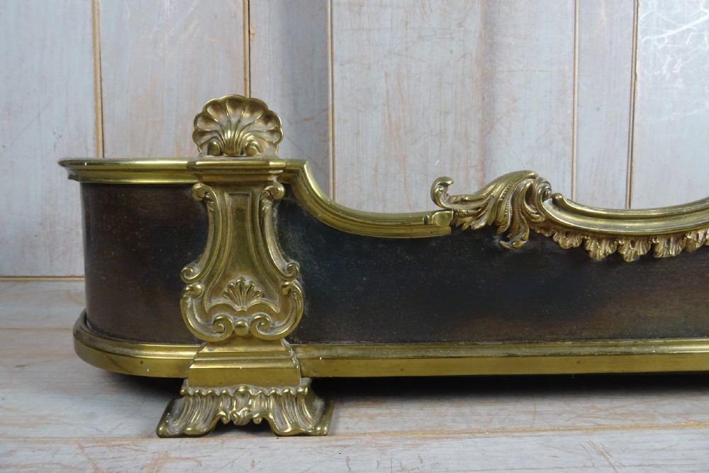 A 19th-century brass and dark steel fireplace fender featuring cast brass Rococo scrollwork and shell motifs along the top rail and corner feet. View VI