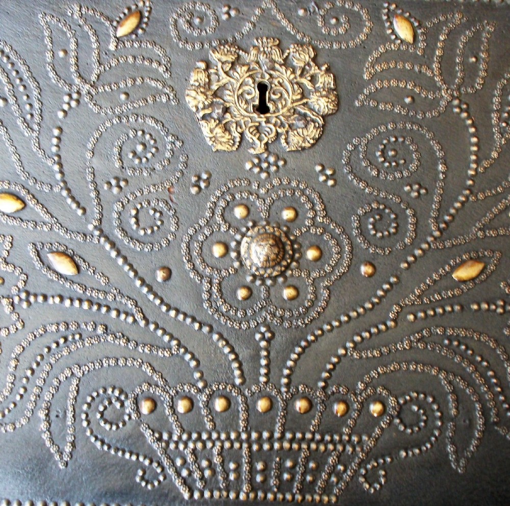 A rectangular dark leather-clad wooden panel adorned with floral and scroll patterns rendered in brass nailhead studs around a central brass escutcheon. View II