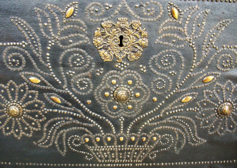 A rectangular dark leather-clad wooden panel adorned with floral and scroll patterns rendered in brass nailhead studs around a central brass escutcheon. View IX