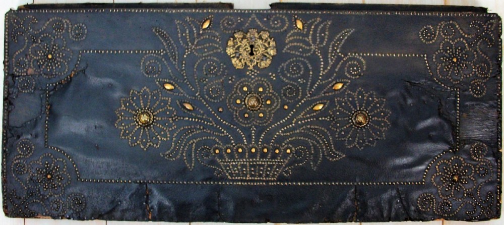 A rectangular dark leather-clad wooden panel adorned with floral and scroll patterns rendered in brass nailhead studs around a central brass escutcheon. View VIII